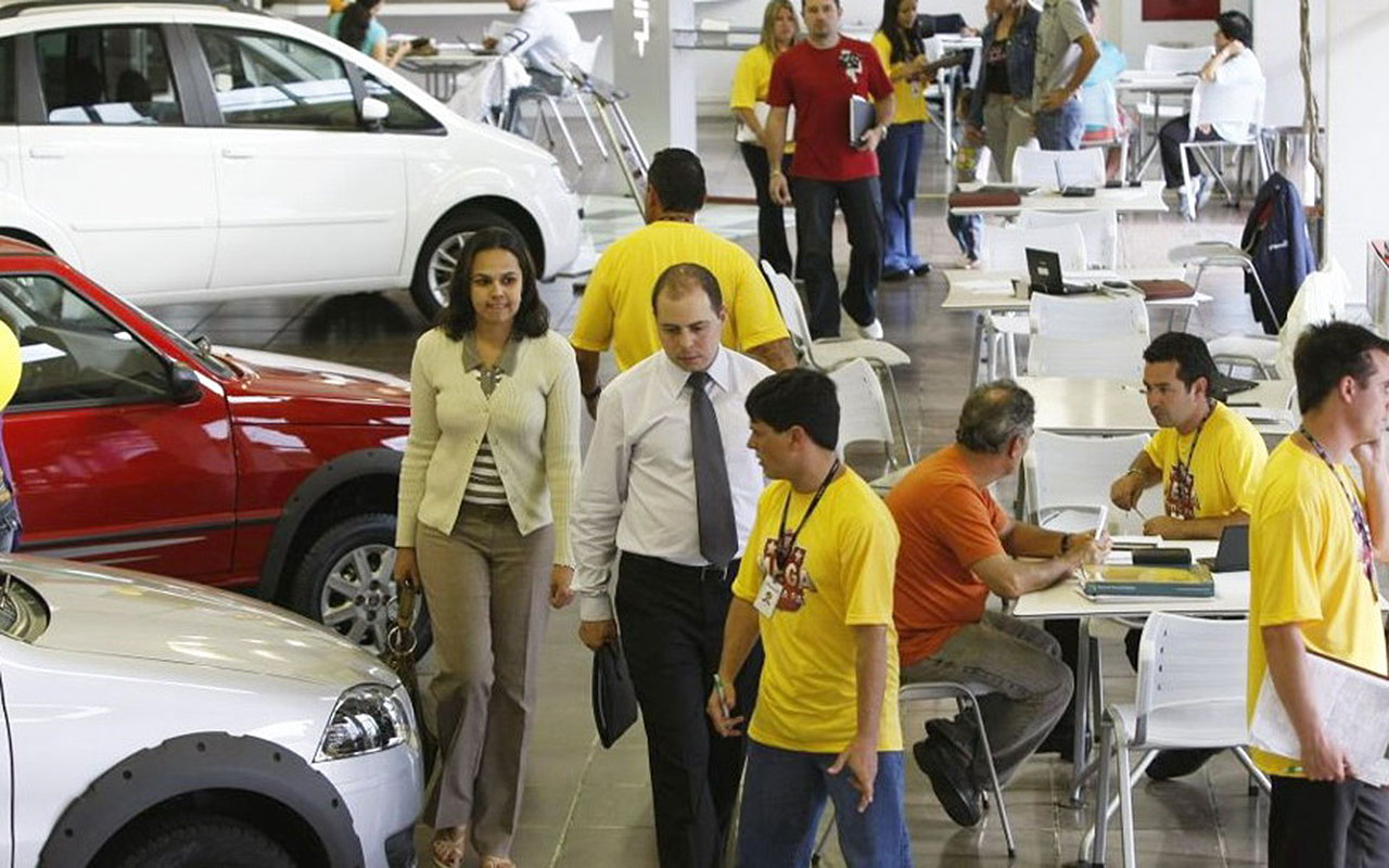 Clientes e vendedores entre veículos e mesas de negociação em uma loja de automóveis