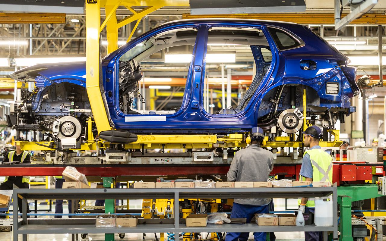Carroceria azul do Geely EX5 EM-i na linha de montagem, com trabalhadores do Complexo Ayrton Senna