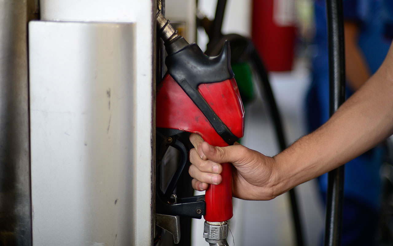 Mão segura bico vermelho de combustível junto à bomba de um posto; foto de arquivo