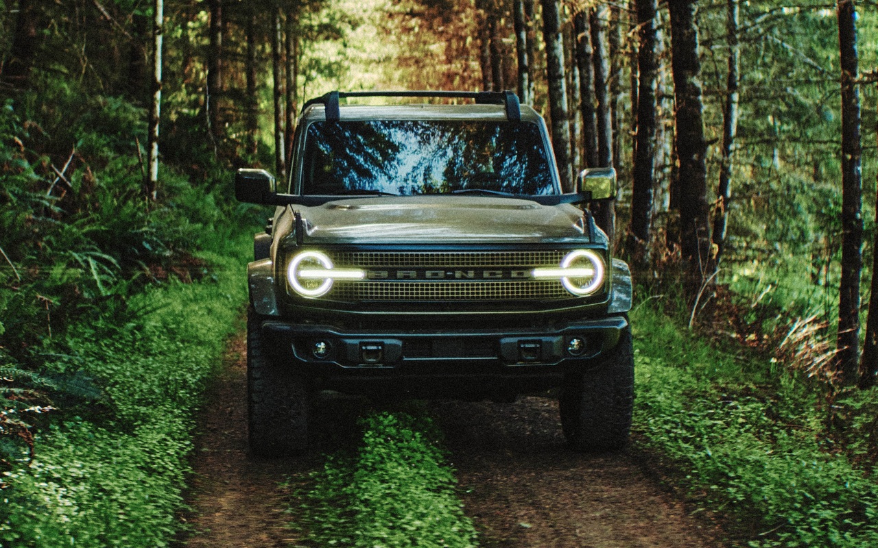 Ford Bronco Filson verde visto de frente em uma trilha na floresta, com faróis acesos