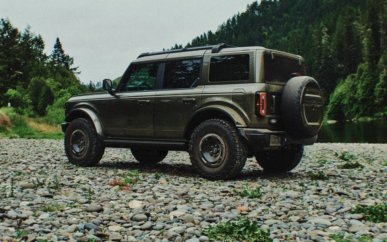 Ford Bronco Filson verde visto de três quartos traseiro sobre terreno pedregoso, com estepe externo