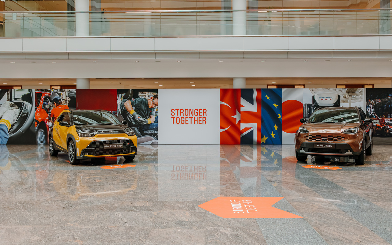 Toyota Aygo X amarelo e Yaris Cross em exposição com bandeiras da Turquia, Reino Unido, União Europeia e Japão