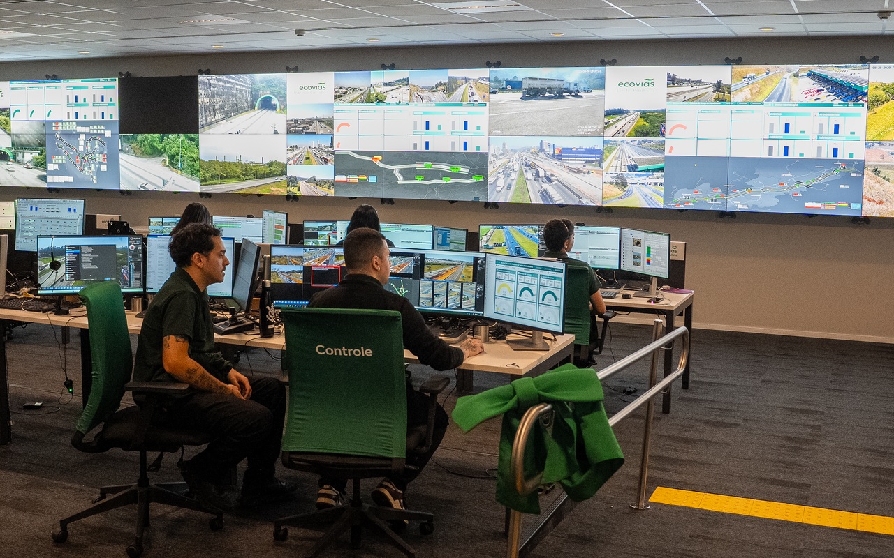 Operadores diante de monitores e de um painel com imagens de rodovias no centro de controle da Ecovias