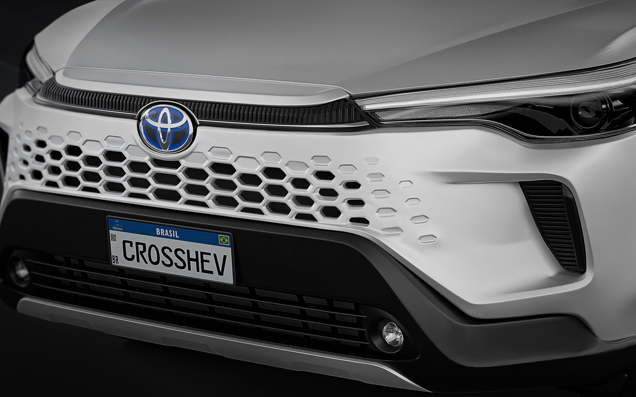 Detalhe da dianteira do Corolla Cross XRV Hybrid branco, com farol e emblema Toyota azul