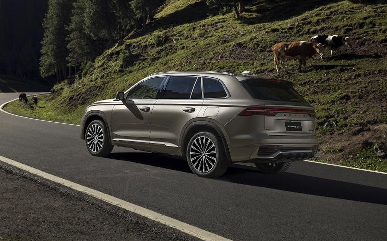 Geely Monjaro EM-i bege em vista três-quartos traseira numa estrada entre montanhas