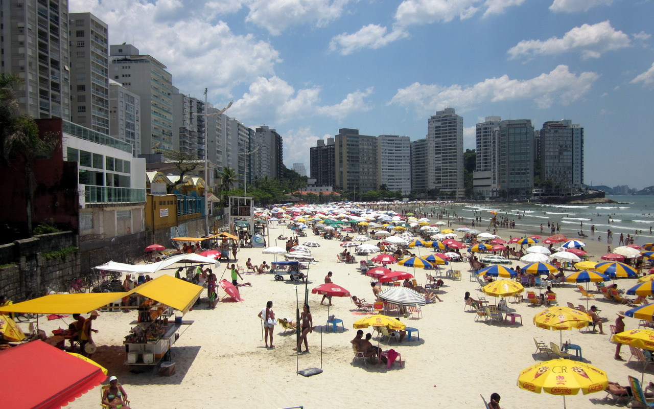 Faixa de areia com guarda-sóis e edifícios na Praia de Pitangueiras, em Guarujá