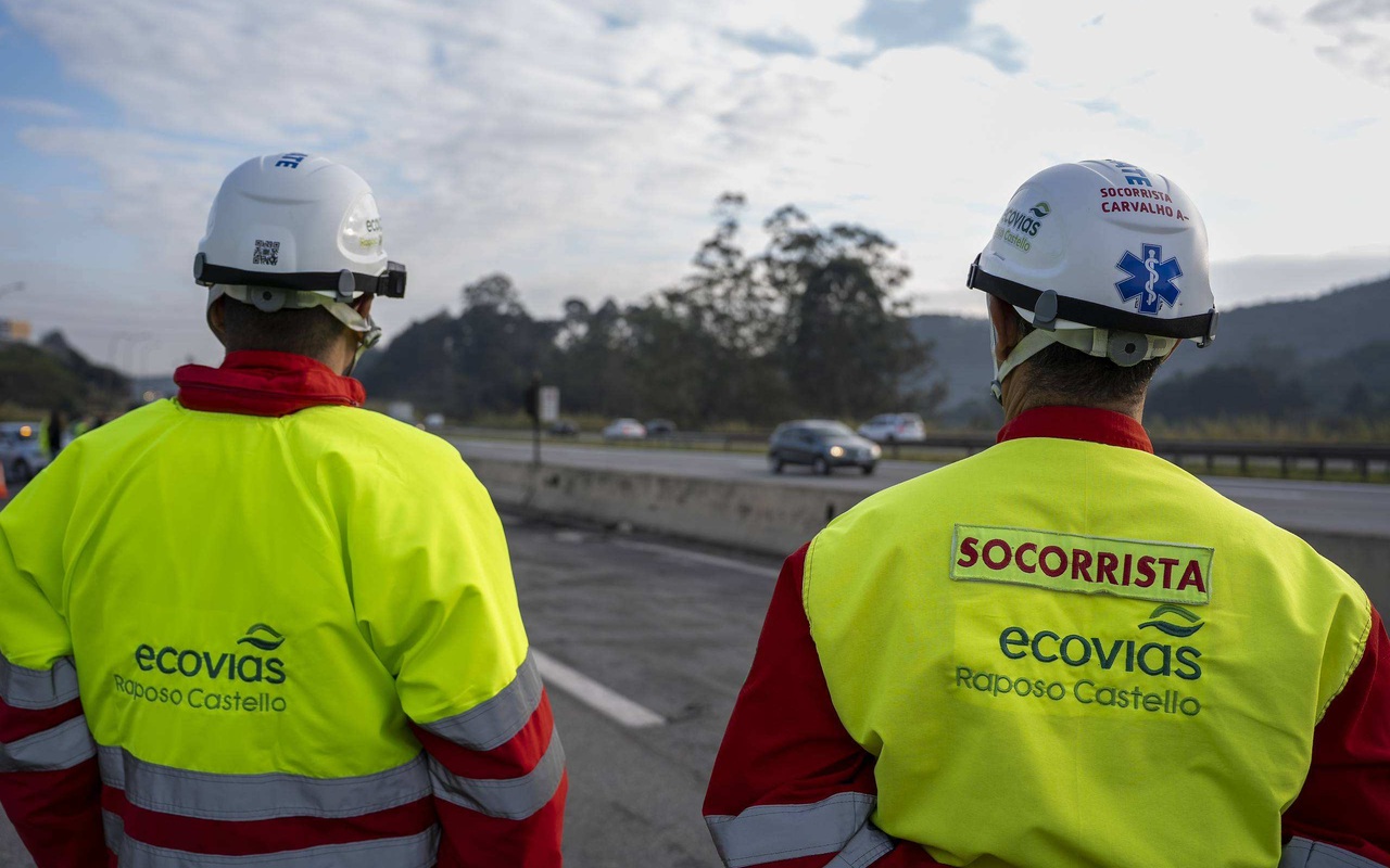 Dois socorristas da Ecovias Raposo Castello vistos de costas, com uma rodovia ao fundo