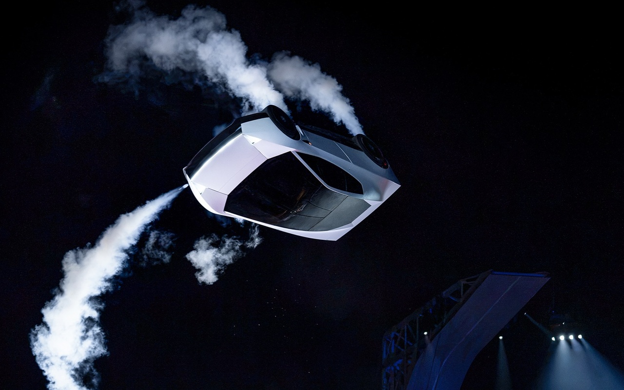 Tesla Roadster invertido no ar, com jatos brancos durante uma manobra